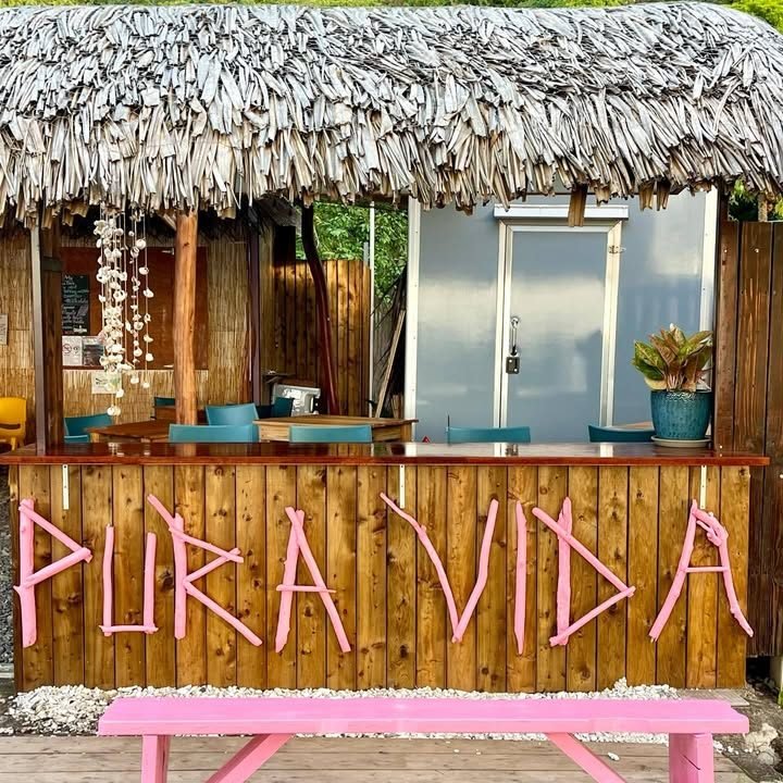 La roulotte Pura Vida : comptoir en bois, lettres roses, toit en pandanus et banc rose